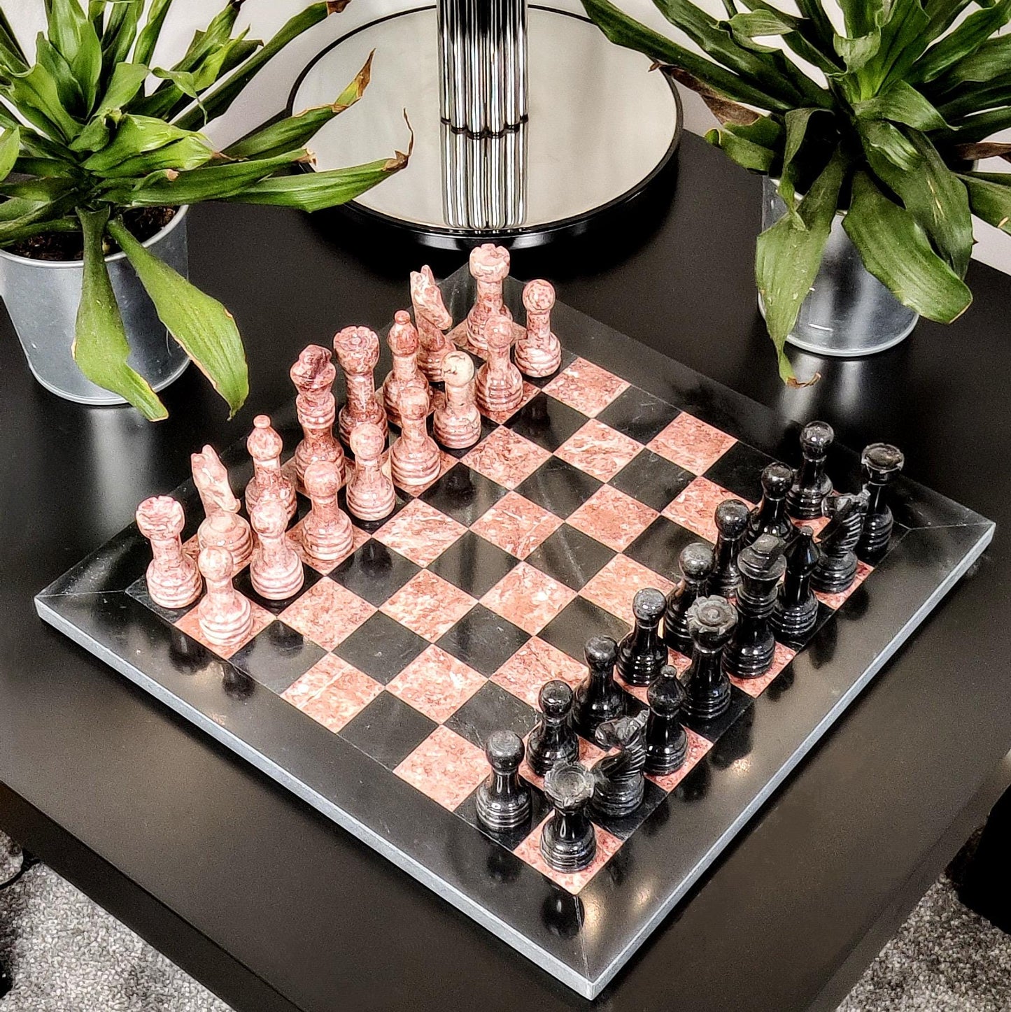 Rose gold and black chess set on a checkered board with plants in the background