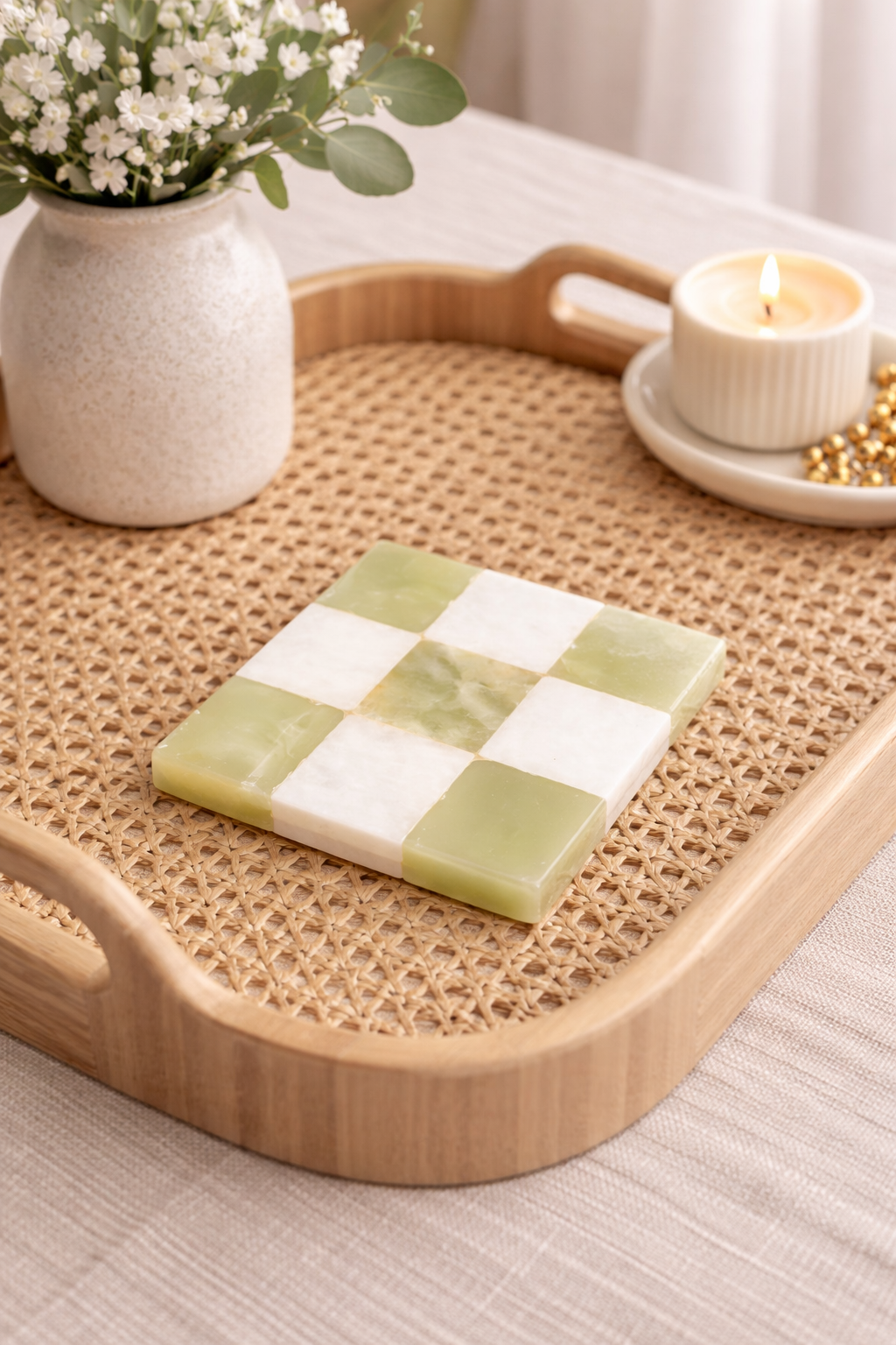 Checkered green and white coaster on a woven tray with a vase and candle in the background.